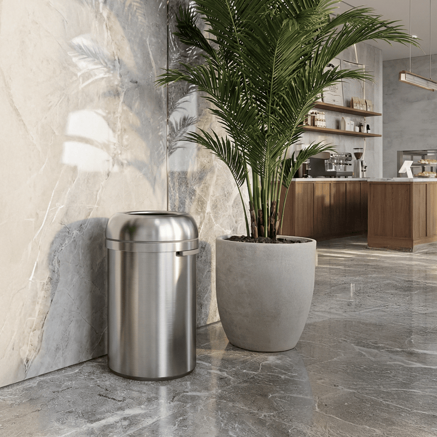 Simplehuman's 115L All-Steel Bullet Open Can in Brushed in a modern cafe setting surrounded by marble walls and floors and a cafe setting in the background.